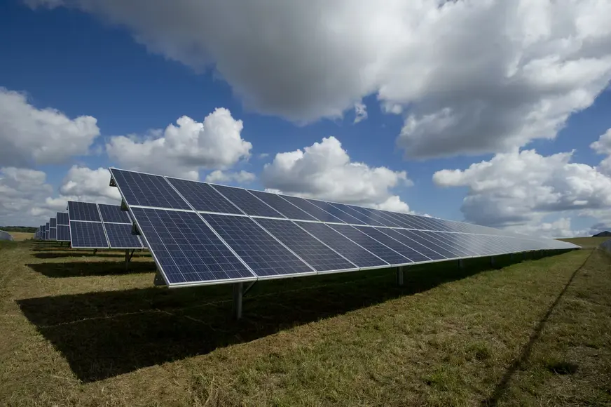 Solar panels in a green field on a partly cloudy day can still generate a significant amount of electricity.