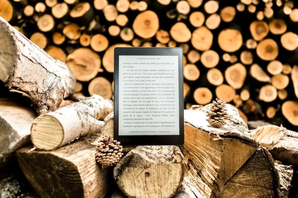 A Kindle sitting on a stack of wood saved by the electronic device. Recycling the device can complete the circle.