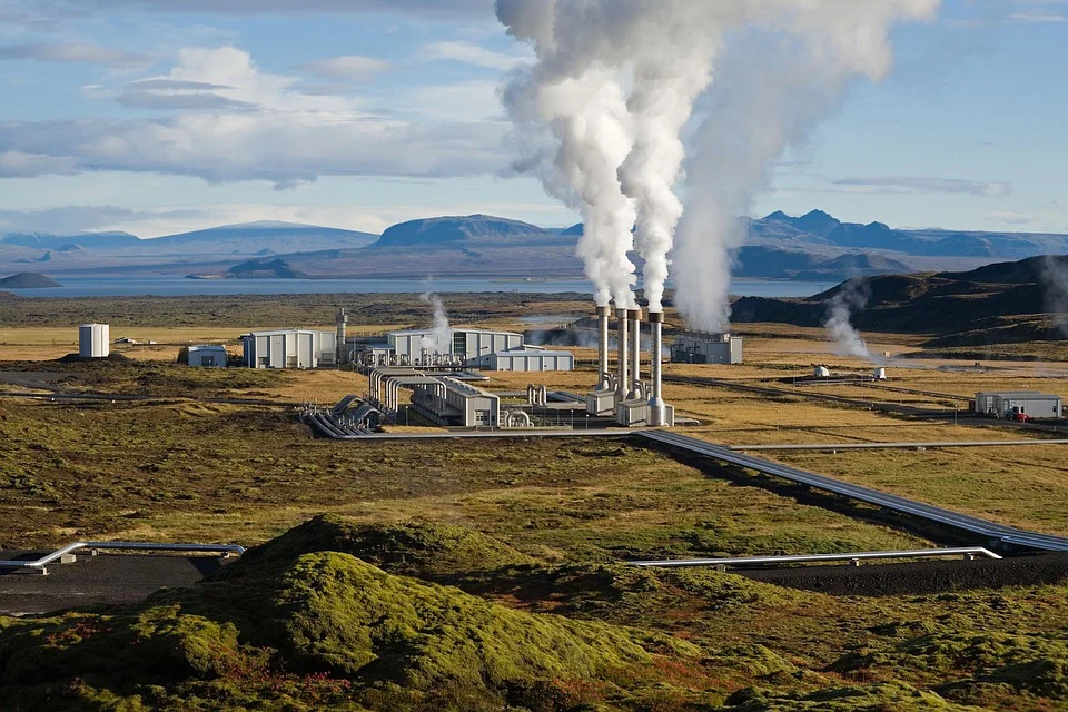 A geothermal power plant located on a lake with steam escaping from generator turbine pipes.