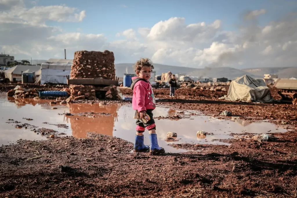 Syrian child standing in the mud of an impoverished refugee camp