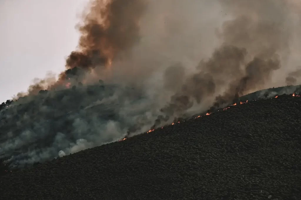 A wildfire burning uphill with plumes of particulates causes thick air pollution.