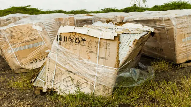 Huge boxes of old, broken solar panels abandoned and left to decay in a green field.