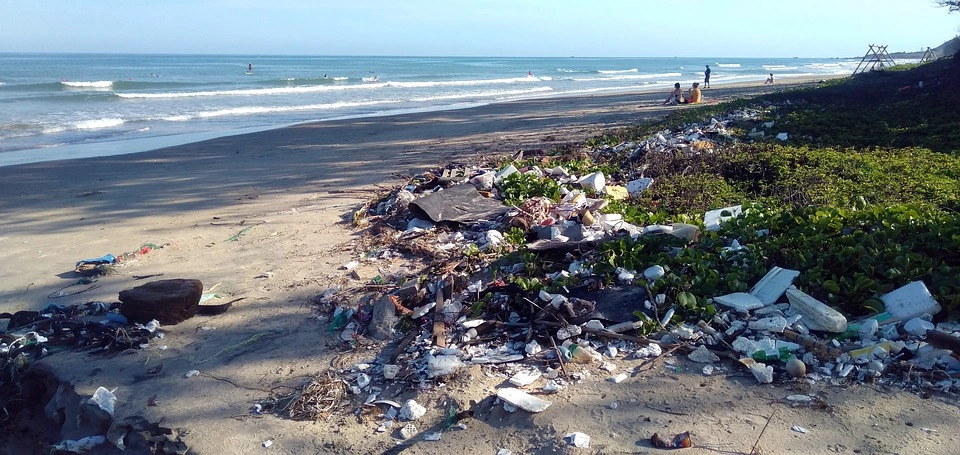 A polluted beach piled with garbage and sun bathers sitting in the sand. 