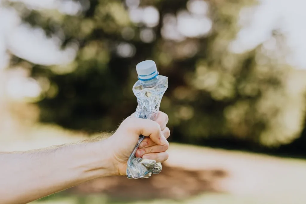 A water bottle made from recycled plastic being crushed by a man's hand.