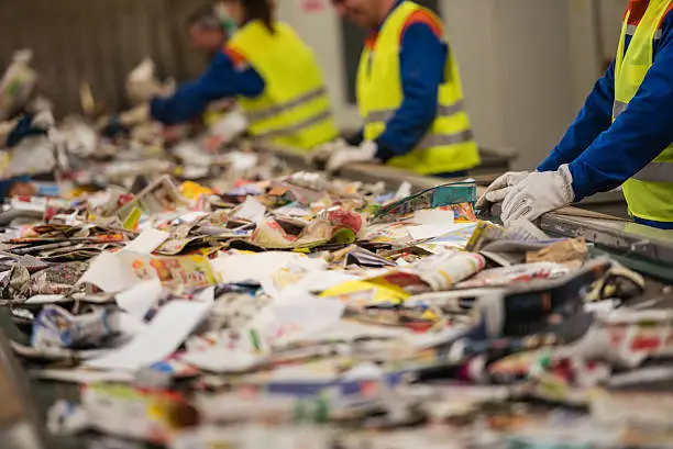 A recycling center conveyor belt with employees sifting through for unsafe or unrecyclable trash.