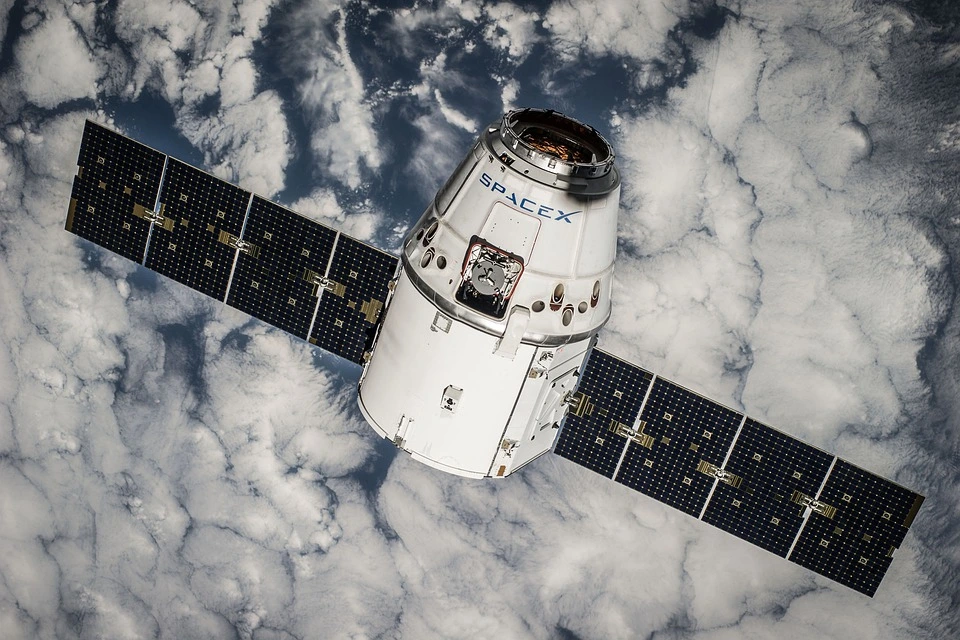 Space X solar satellite orbiting the earth with clouds in the background.