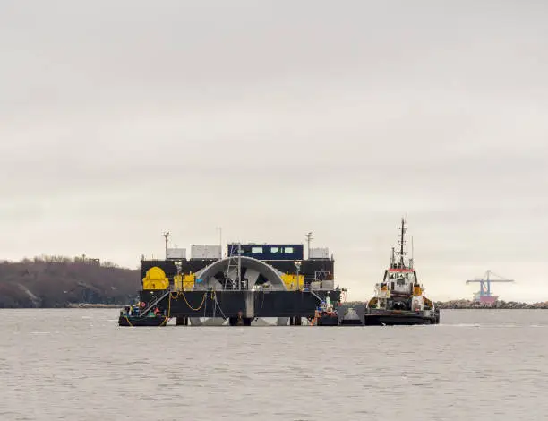 A tidal energy turbine on a barge being tugged to sea for installation in a tidal energy project.