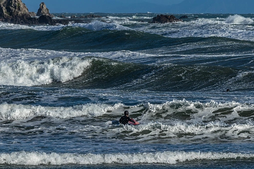 A man surfing in the turbulent ocean tide with rocks in the distance