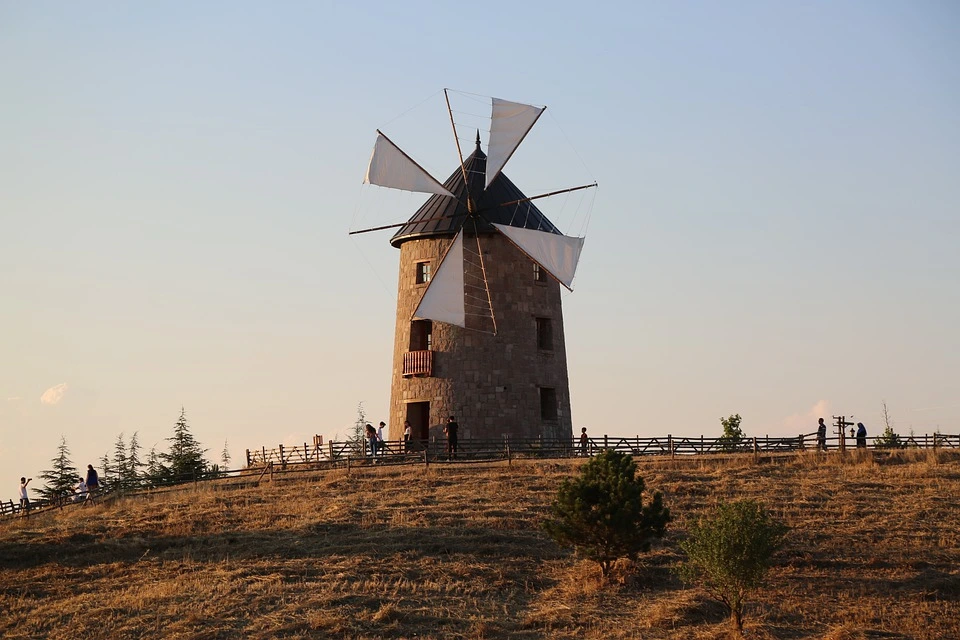 An ancient windmill on a hill with tourists observing the ancient technology.