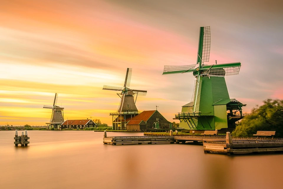 3 windmills on a lake in the sunset are traditionally used for milling grain and pumping irrigation water.